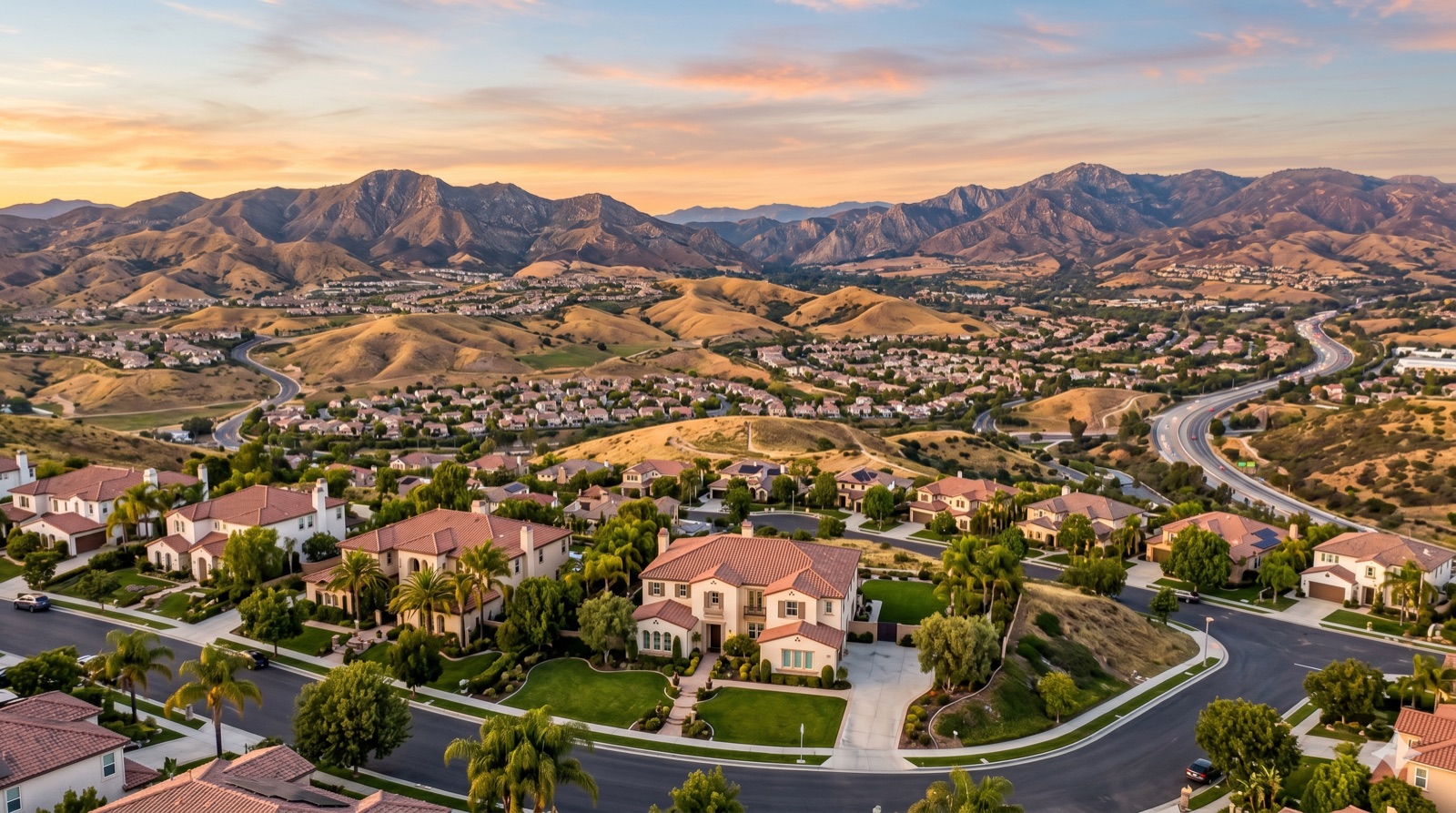 Aerial view of a Santa Clarita Valley neighborhood at sunset with the surrounding mountains